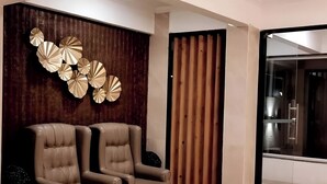A modern room with two leather armchairs, a wooden wall with decorative panels, and a glass door leading to a bathroom. - Ashwa Glory Retreat (Igatpuri)