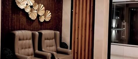 A modern room with two leather armchairs, a wooden wall with decorative panels, and a glass door leading to a bathroom.
