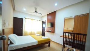 A hotel room with a bed, a chair, a television, and a ceiling fan. - Nandan Residency  (Mysore)