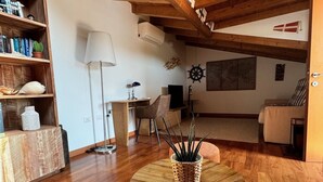 A cozy living room with wooden floors, a round wooden coffee table with a woven basket, a bookshelf, a lamp, and a flag on the wall. - Oasis beach & golf Apartment nestled in nature next to the beach (Venezia)