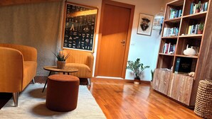 A cozy living room with a wooden floor, a sofa, a small table, and a bookshelf filled with books and plants. - Oasis beach & golf Apartment nestled in nature next to the beach (Venezia)