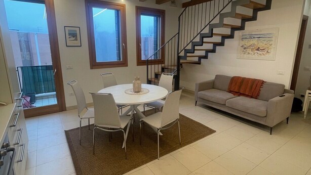 A spacious living area with a dining table, sofa, and a staircase leading to an upper floor. - Oasis beach & golf Apartment nestled in nature next to the beach (Venezia)