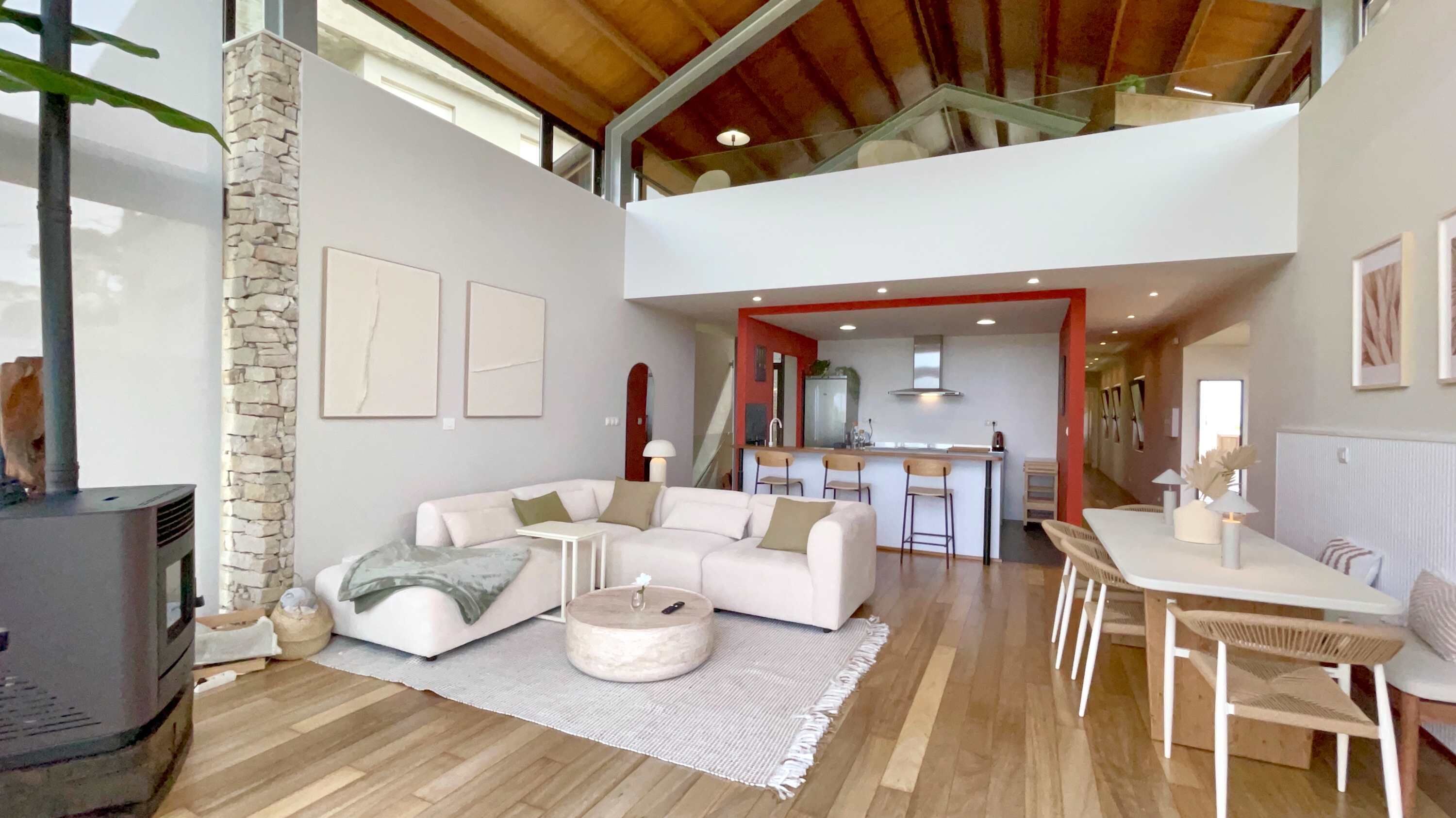 A spacious living area with a high ceiling, a stone wall, and a modern kitchen in the background.