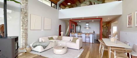 A spacious living area with a high ceiling, a stone wall, and a modern kitchen in the background.