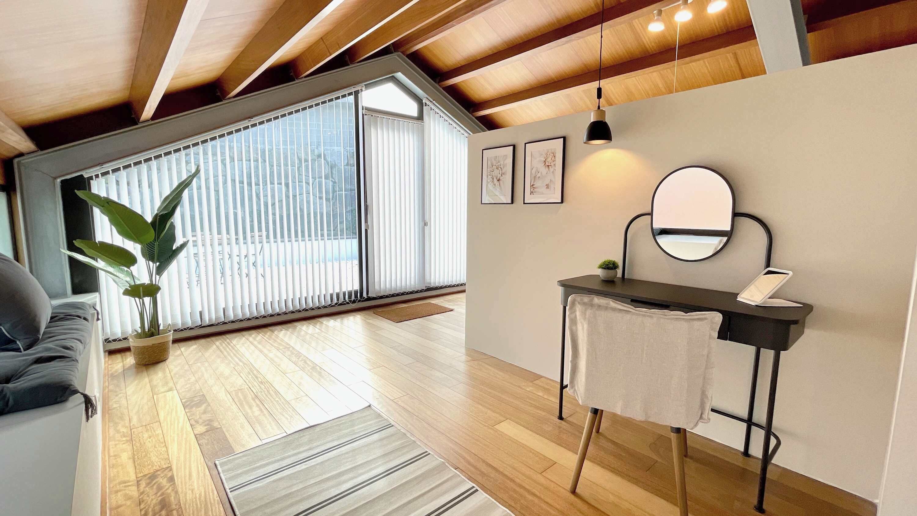 A modern living room with a wooden ceiling, a sofa, a plant, a small table with a mirror, and a view through large windows.