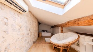 A cozy attic bedroom with a skylight, a wicker chair, and a bed with a white headboard.