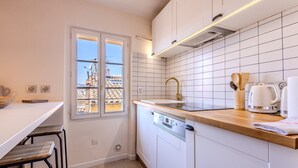 A modern kitchen with white cabinetry, a wooden countertop, a built-in dishwasher, and a window with a city view.