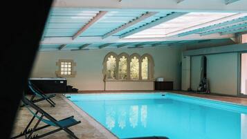 A swimming pool with a view of a building's interior, including a window with a decorative arch and a ceiling with skylights.