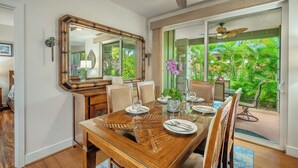 Comedor con una gran mesa de madera dispuesta para seis personas, un espejo grande y vistas a vegetación exuberante a través de puertas de vidrio.