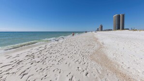 Una playa con huellas, cielo despejado y edificios altos al fondo.