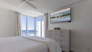 Un dormitorio con cama, cómoda, televisor y vista al océano.