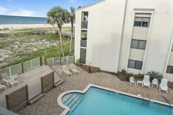 A pool area with lounge chairs, a wooden deck, and a view of the beach.