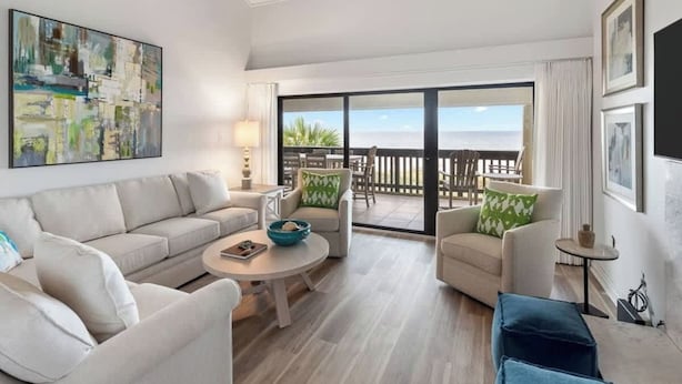 Una sala moderna con un sofá, sillones, una mesa de centro y un balcón con vistas al océano.