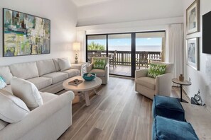 Ein modernes Wohnzimmer mit einer Couch, Sesseln, einem Couchtisch und einem Balkon mit Meerblick.