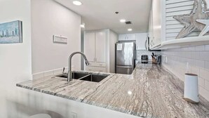 Cocina moderna con encimera de mármol, electrodomésticos de acero inoxidable y salpicadero blanco.
