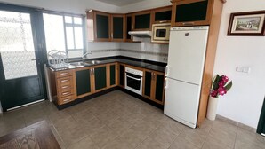A kitchen with wooden cabinets, a white refrigerator, a microwave, and an oven. - HOUSE LA ESTRELLA PLAYA BLANCA LANZAROTE (Playa Blanca)