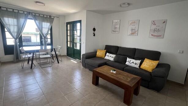 A living room with a grey sofa, a wooden coffee table, and a dining area with a table and chairs. - HOUSE LA ESTRELLA PLAYA BLANCA LANZAROTE (Playa Blanca)
