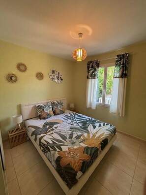 Een slaapkamer met een bed, een plafondlamp, een raam met gordijnen en wanddecoraties.