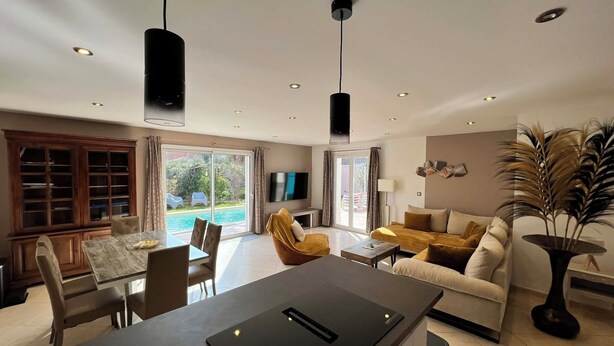 Un salon moderne comprenant un coin repas, un téléviseur à écran plat et une grande fenêtre donnant sur une piscine.