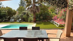 Un espace patio avec une piscine, des meubles en osier et une vue sur la piscine et le jardin.