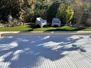 Een terras met twee witte stoelen, een houten vloer, een tuin met diverse planten en een houten hek.