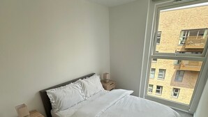 A bedroom with a large window, a bed, a nightstand, and a wall-mounted light fixture. - London Bliss Apartment Retreat (London)