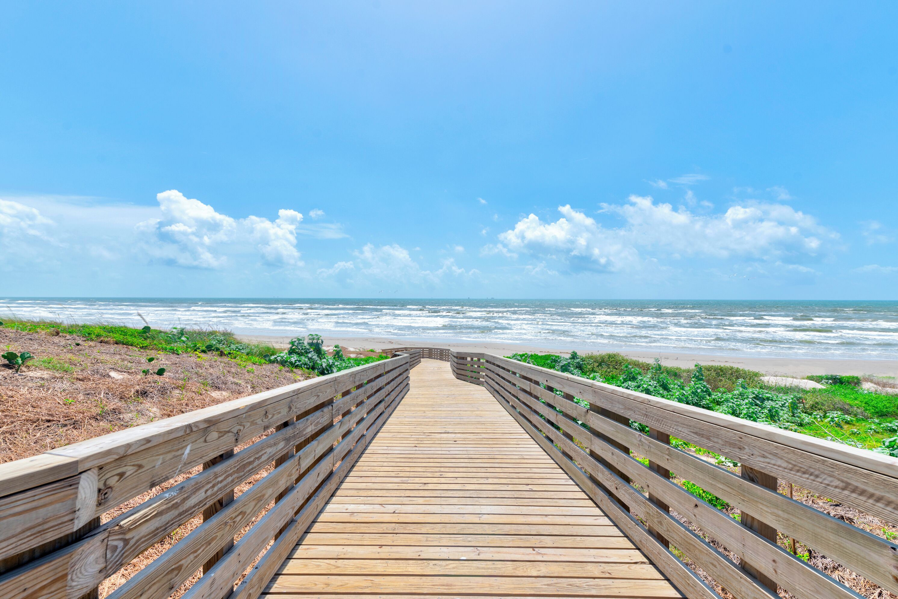 A wooden boardwalk leading to the beach with a clear view of the ocean and sky.
