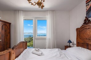 A bedroom with a large window, a wooden bed, a nightstand, and a chandelier. - Hidden Pool House With Sea View (Novi Vinodolski)