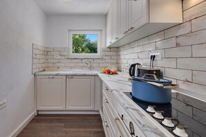 A compact kitchen with white cabinets, a window, and a stove. - Hidden Pool House With Sea View (Novi Vinodolski)