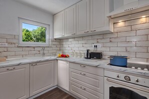 A kitchen with white cabinets, a window, and a stove. - Hidden Pool House With Sea View (Novi Vinodolski)