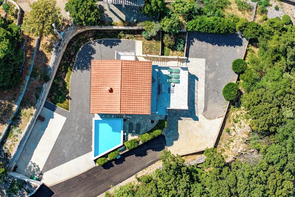 An aerial view of a property with a swimming pool, a covered patio, and a stone facade.
