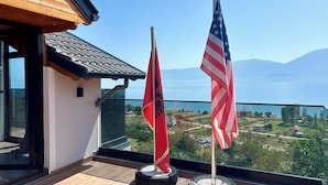 Un balcon orné de deux drapeaux, avec vue sur un lac et un paysage montagneux.