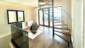 Un intérieur moderne avec un escalier en colimaçon, un téléviseur à écran plat et une vue dégagée grâce à de grandes fenêtres.