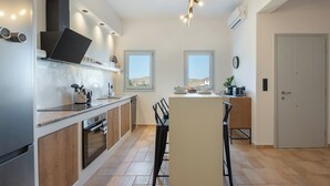 Una cucina moderna con isola centrale, forno integrato ed elettrodomestici in acciaio inossidabile. Due finestre offrono luce naturale e vista sull'esterno.