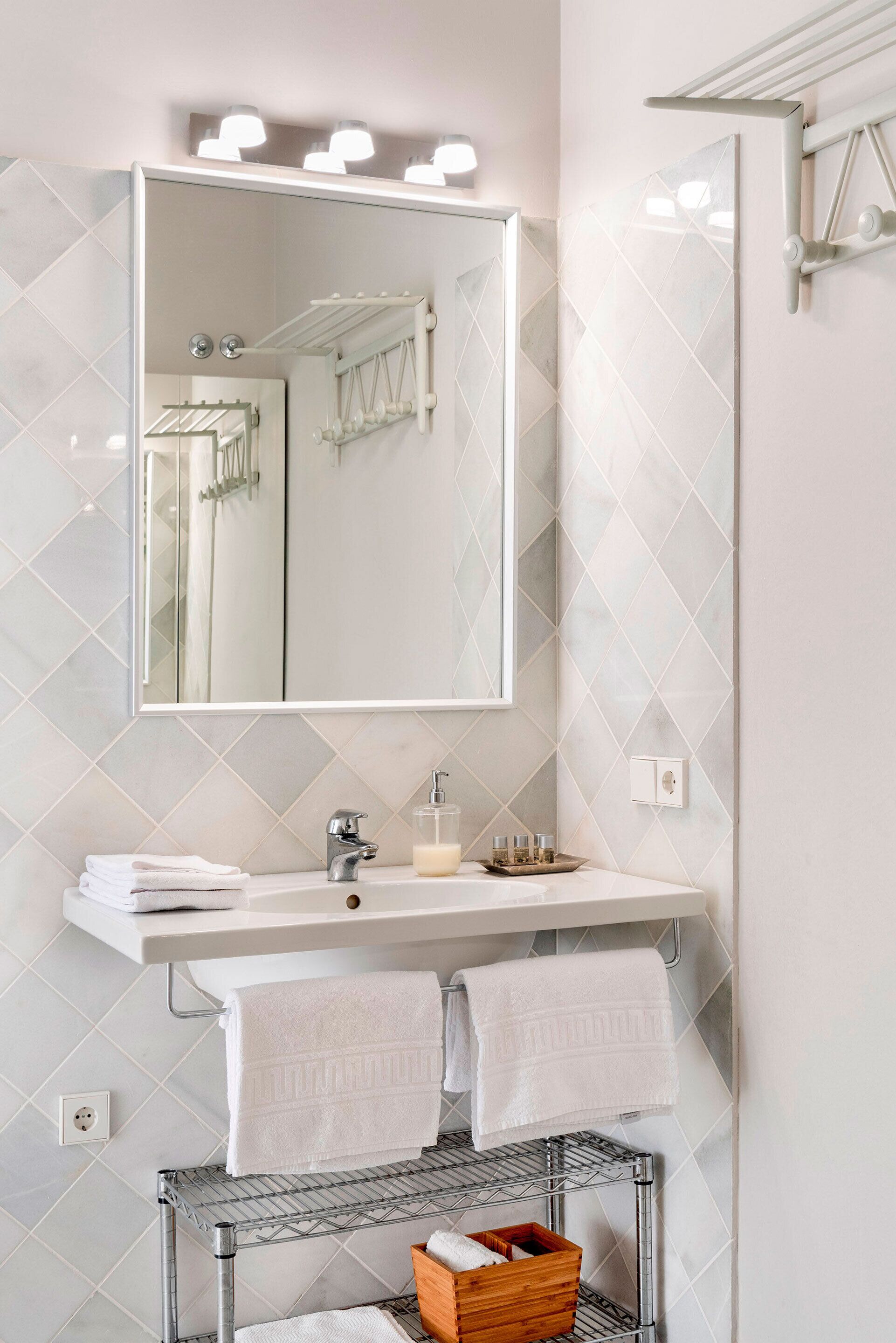 Un bagno moderno con uno specchio grande, piastrelle bianche, un mobile lavabo e un portasciugamani.
