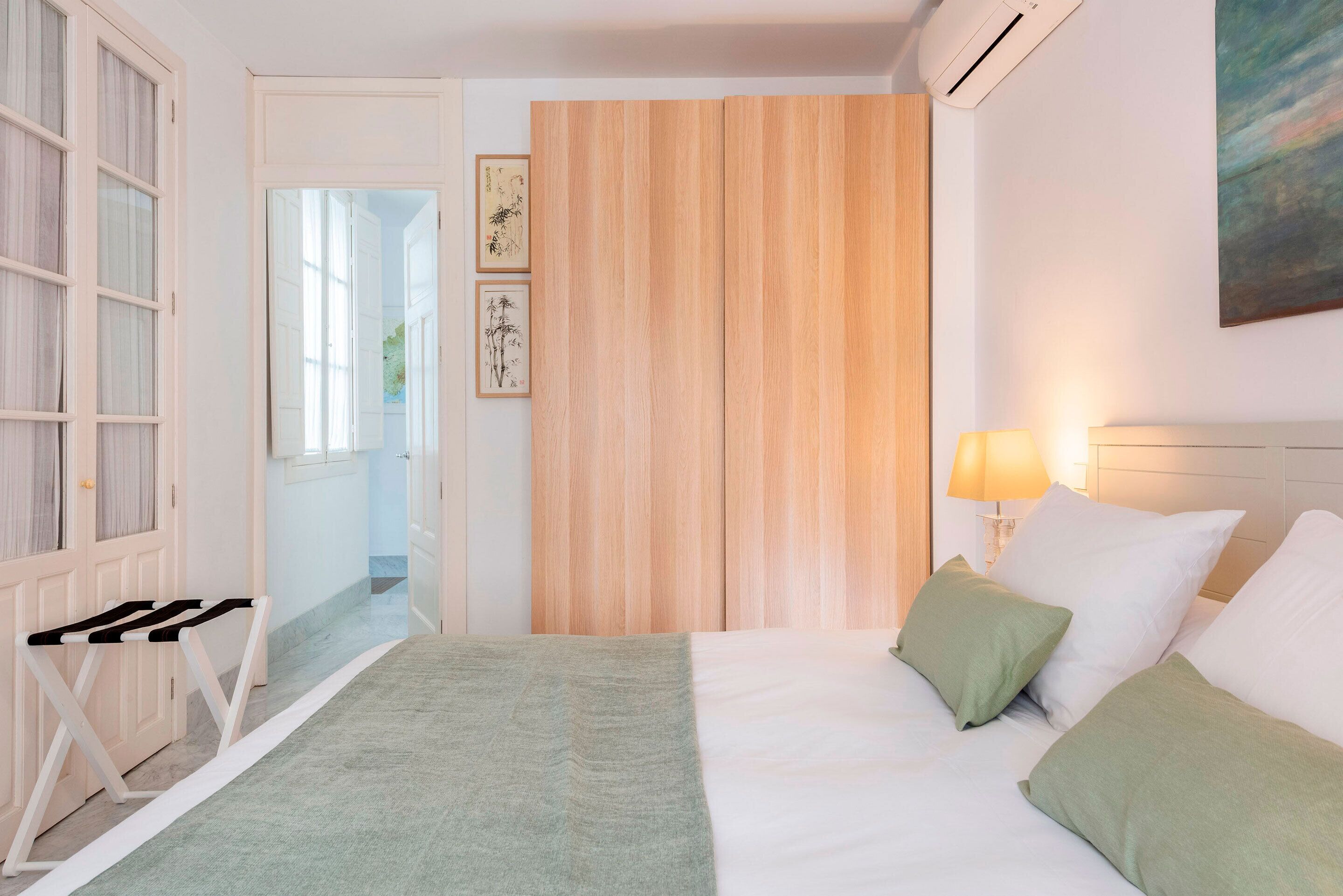 A hotel room with a bed, a bedside table, a lamp, and a view of the hallway.
