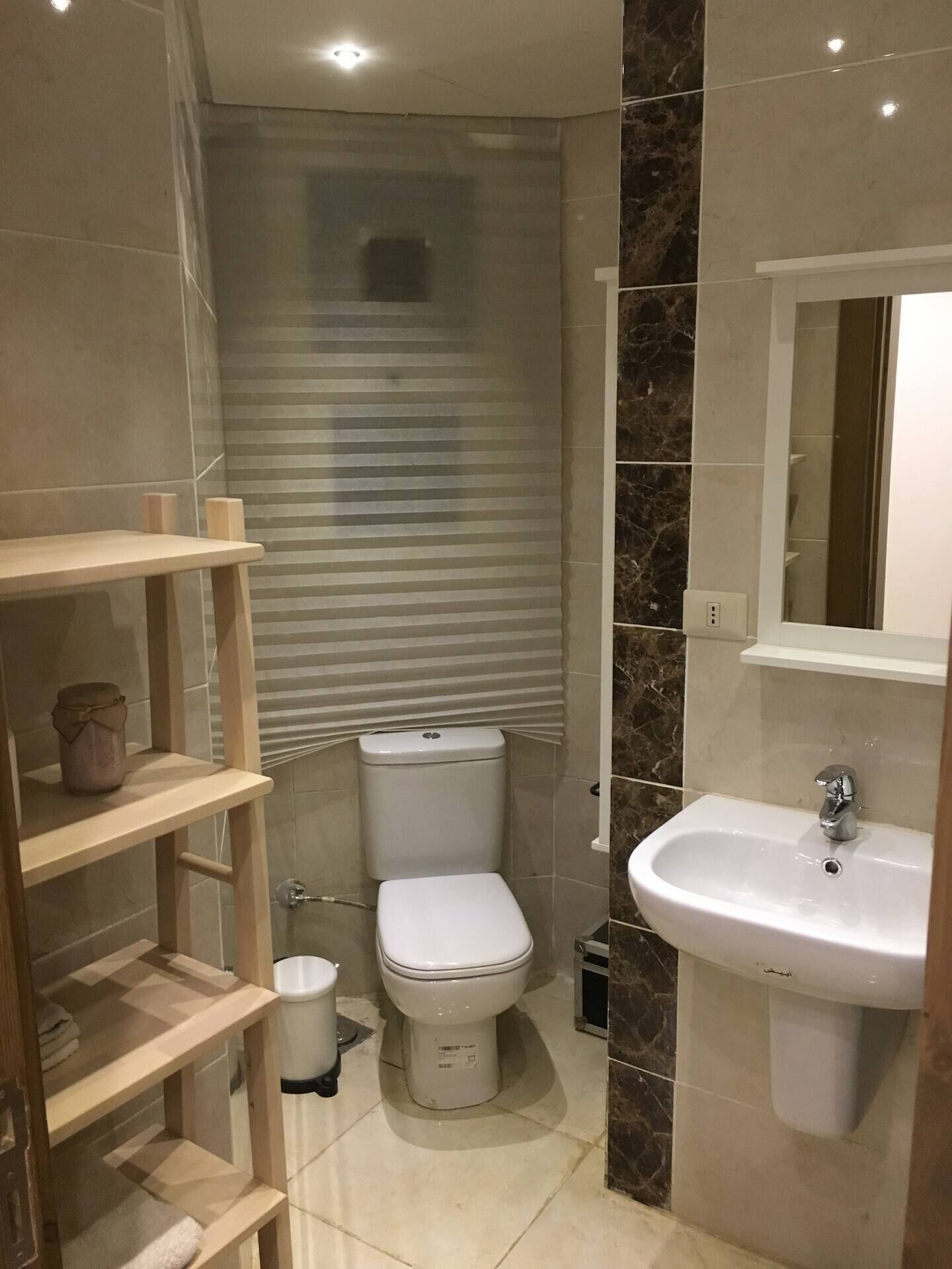 Une salle de bain avec des toilettes, un lavabo et une étagère en bois sur laquelle se trouve un pot.