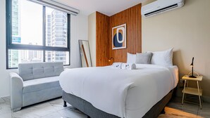 Una habitación de hotel moderna con una cama grande, un sofá, una pared decorativa de madera y vistas a la ciudad.