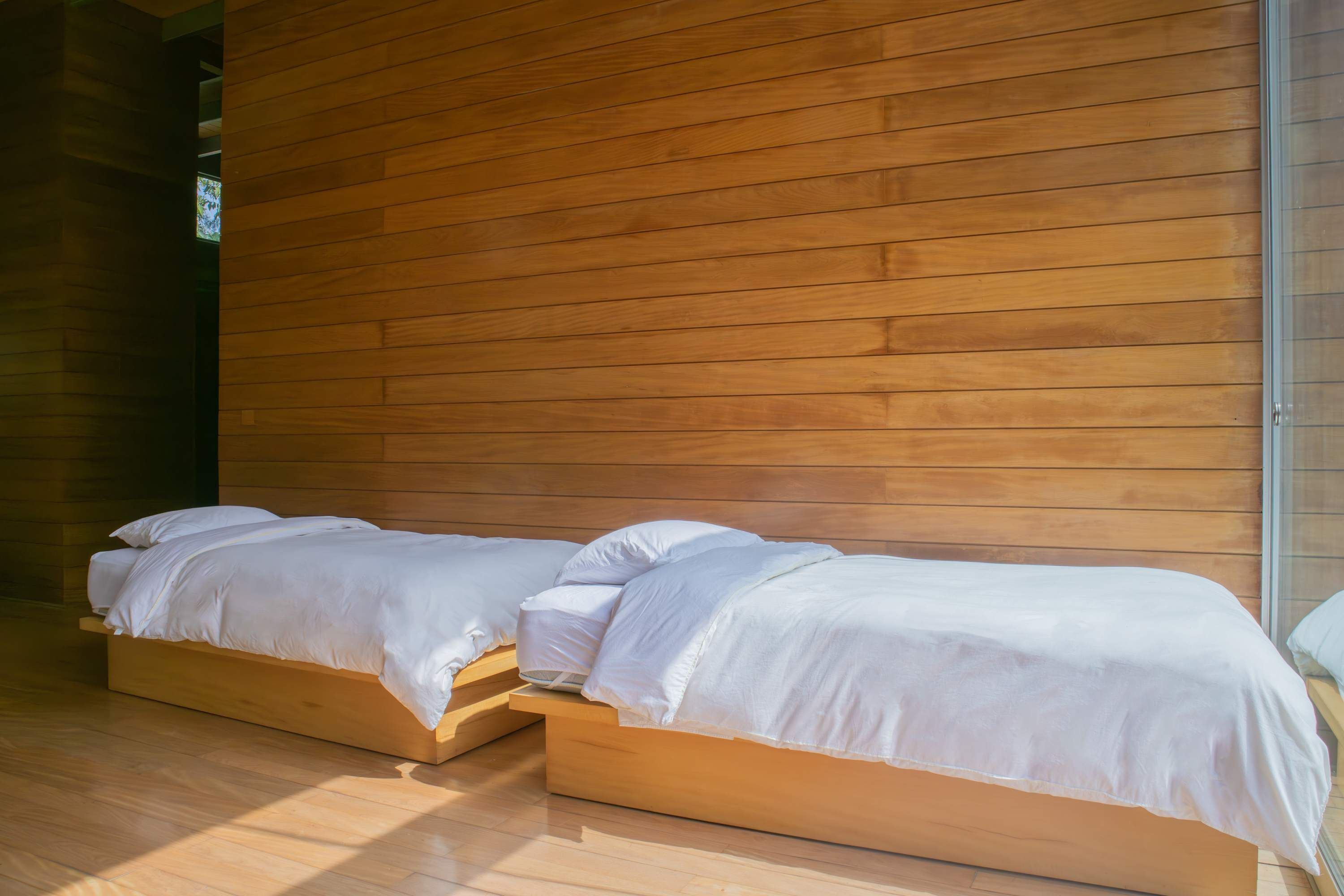 A modern bedroom with a wooden slatted wall, a wooden bed frame, and a wooden floor.