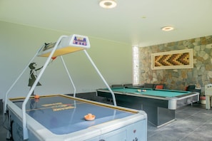 A pool table with a pool cue rack, a billiards table, and a stone wall with a pixelated artwork. - w Elegant 5BR Home w Pool in Cieneguilla (Pachacámac)