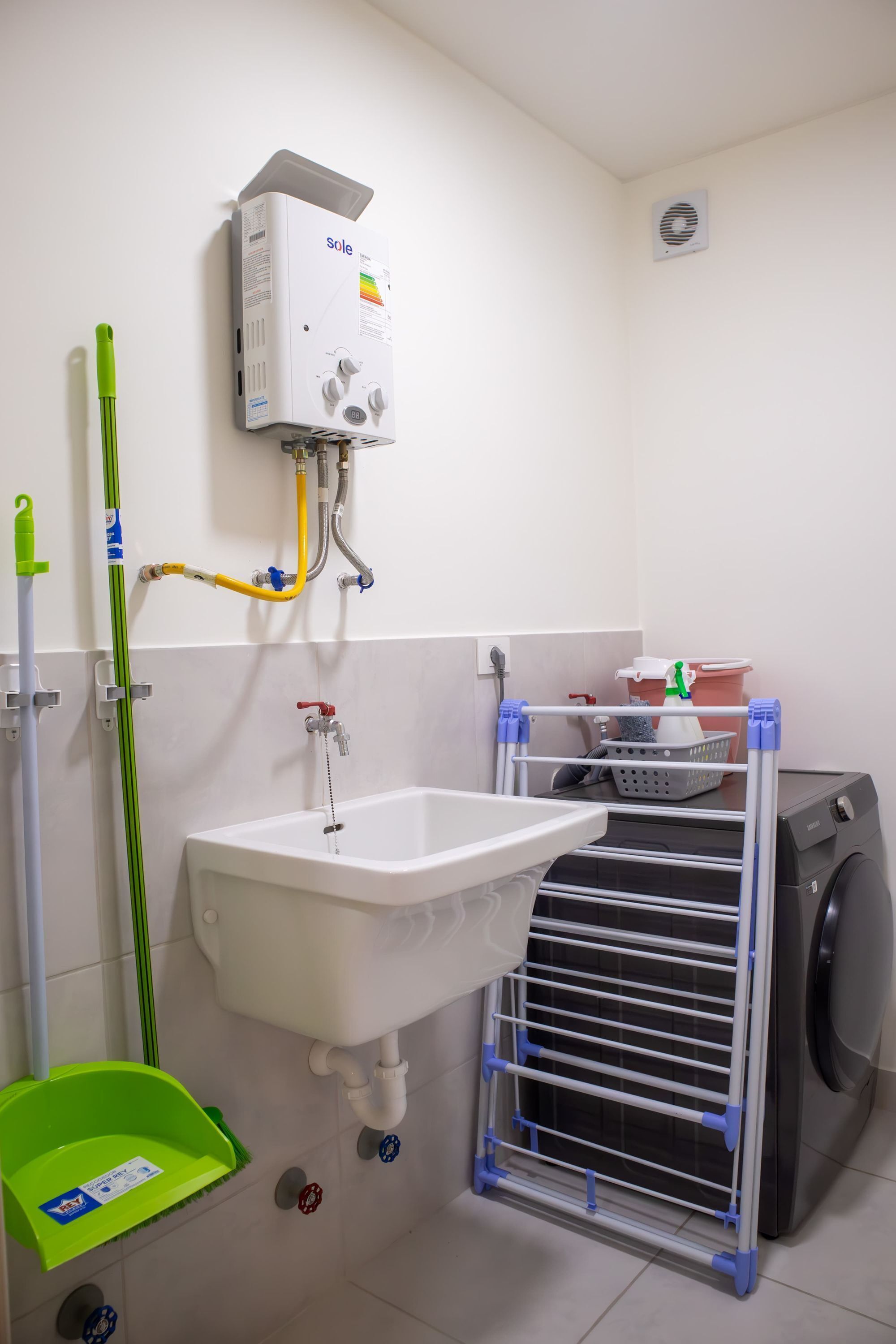 A bathroom with a white sink, a green mop, a washing machine, and a laundry rack.