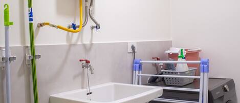 A bathroom with a white sink, a green mop, a washing machine, and a laundry rack.