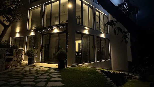 Una casa moderna de dos pisos con amplios ventanales, un sendero de piedra y una entrada bien iluminada.
