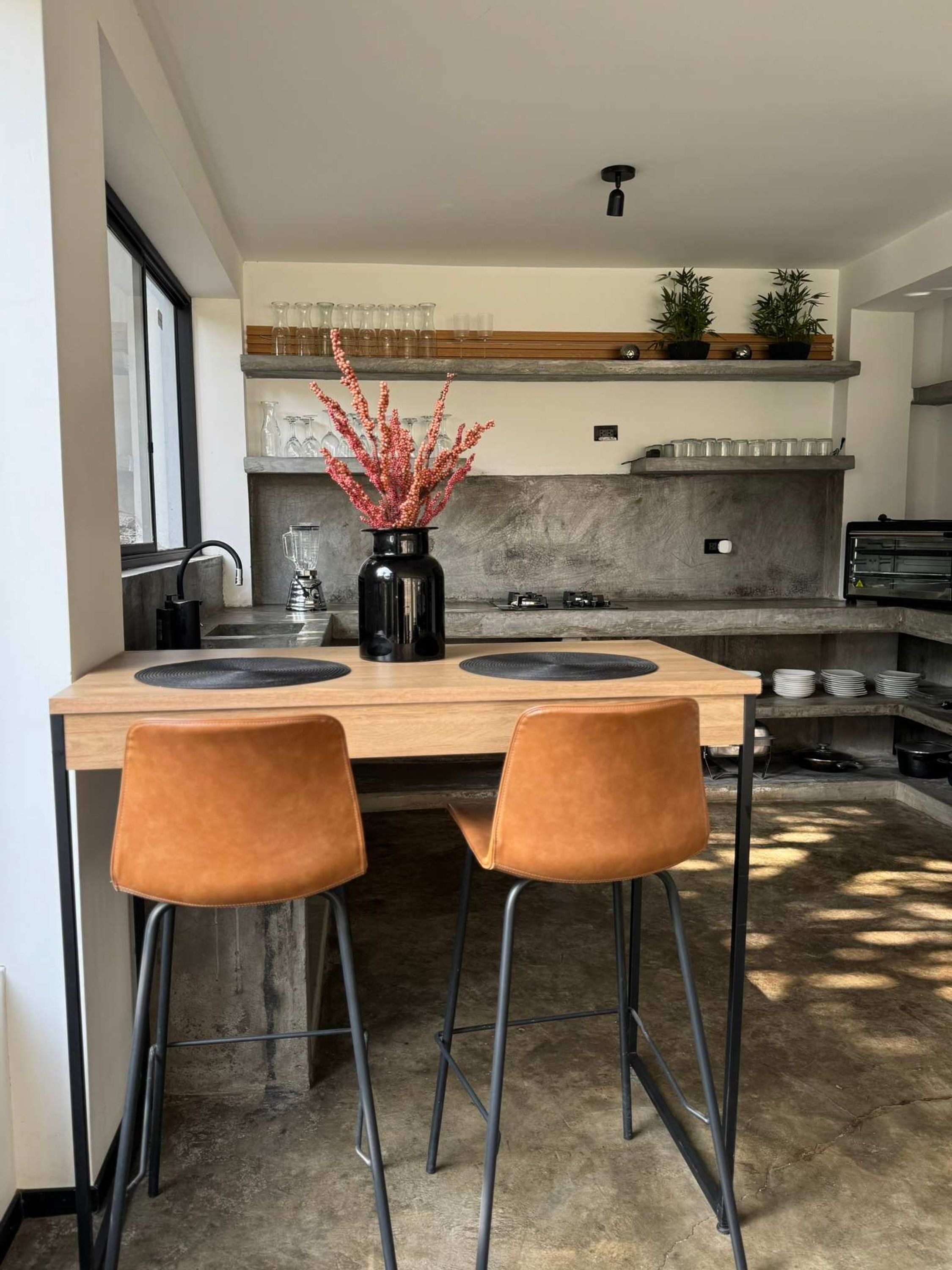 Une cuisine moderne avec un îlot central en bois, deux chaises marron, un vase noir orné de fleurs rouges et un four encastré.