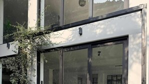Un edificio moderno con amplios puertas correderas de vidrio, un patio empedrado de piedra y dos plantas en macetas.