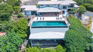 A large, modern house with a swimming pool, surrounded by lush greenery and a rocky landscape. - w Breathtaking 9BR Villa in Costa Rica (Cabo Velas)