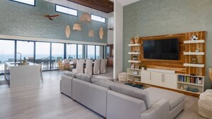 A spacious living area with a large TV, wooden shelves, and a view of the ocean. - w Breathtaking 9BR Villa in Costa Rica (Cabo Velas)
