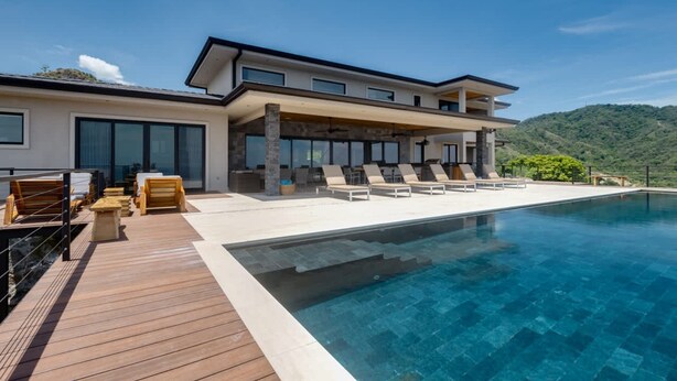 A modern two-story house with a pool, wooden deck, and lounge chairs. - w Breathtaking 9BR Villa in Costa Rica (Cabo Velas)