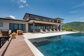 A modern two-story house with a pool, wooden deck, and lounge chairs. - w Breathtaking 9BR Villa in Costa Rica (Cabo Velas)