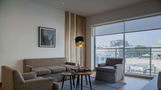A modern living room with a large window, a sofa, a coffee table, and a lamp. - Stunning 1BR With Great Deco in Miraflores (Lima)